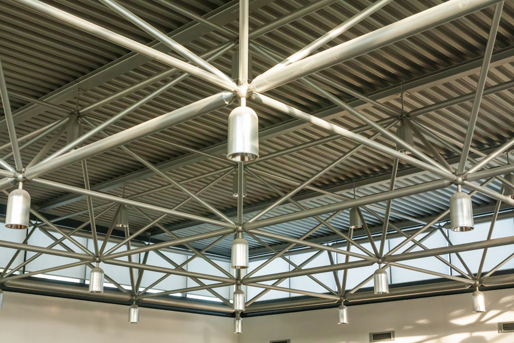 Exposed metal ceiling beams and hanging cylindrical lights in a modern industrial-style building interior.